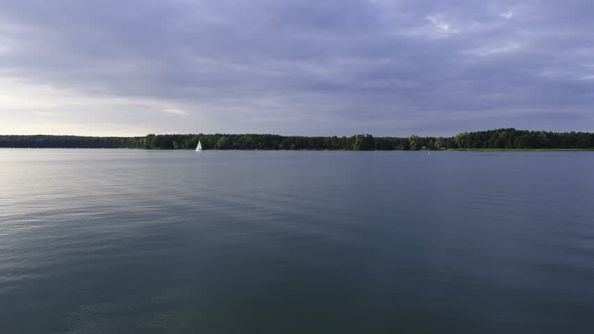 A wide-angle shot of a tranquil Masurian lake glowing with warm evening light, reflecting soft clouds across a smooth glass-like surface