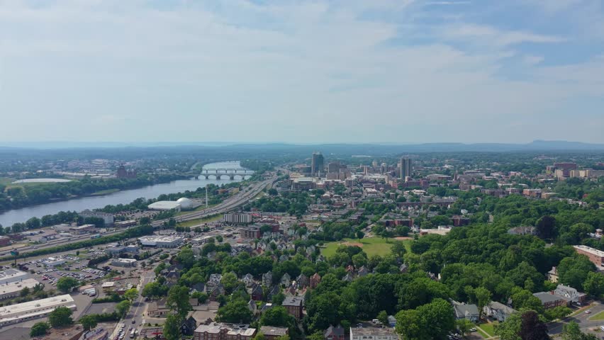 Distant drone shot of Springfield city skyline stretches along the Connecticut River with 91 highway and bridges running through leafy neighborhoods on summer, Massachusetts, US