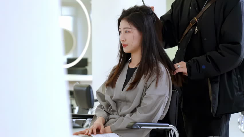 Young woman client getting trendy haircut from designer hair stylist, hairdresser talking consults with customer for service, grooming or comb hairstyle at light salon or barber shop business