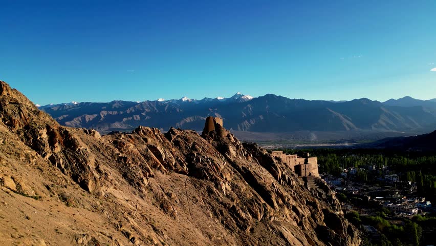 Aerial view of Leh Palace perched on a rocky ridge with the Himalayan mountain range in the background under a clear blue sky in Leh, Ladakh, India.
