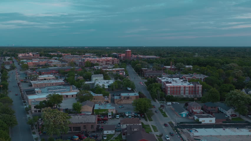 Blue-hour aerial of Highland Park, Illinois — the downtown core and landmark brick water tower surrounded by deep tree canopy on Chicago