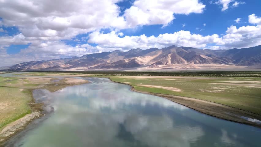 Aerial view of the Indus River flowing through the rugged landscape of Dungti with mountains and reflective clouds in the sky in Dungti, Ladakh, India.