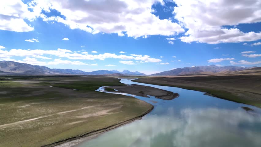 Aerial view of the Indus River winding through the arid landscape of the high altitude desert with distant mountains under a blue sky in Dungti, Ladakh, India.