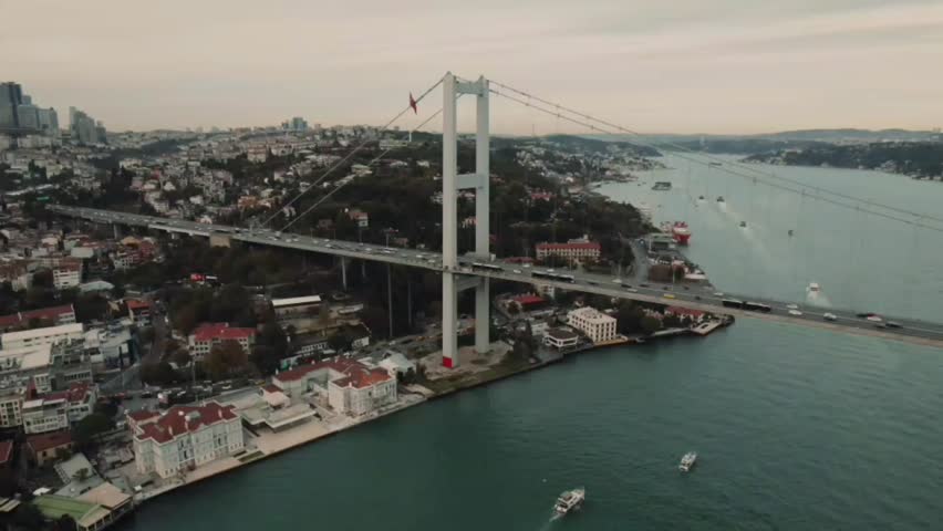 Not AI Generated. 4K aerial view of the Bosphorus Bridge in Istanbul, Turkey, featuring moving traffic, boats crossing the Bosphorus Strait, a scenic waterfront skyline, and a panoramic urban landscape during the evening. Suitable for travel, tourism, transportation, architecture, and editorial projects.