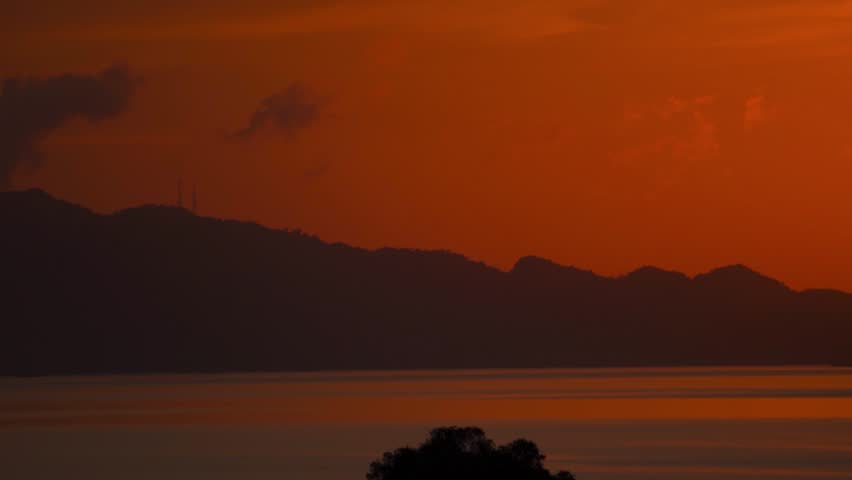 Fiery red sun setting above hills in ocean at Langkawi island, Malaysia. Sunset over sea at dawn. Serene nature landscape. Travel and summer holidays concept.