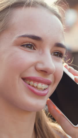 Beautiful smiling woman talking on cell phone answering frends call when leans on her modern car which is parked by area house. Outdoors. Slow motion.