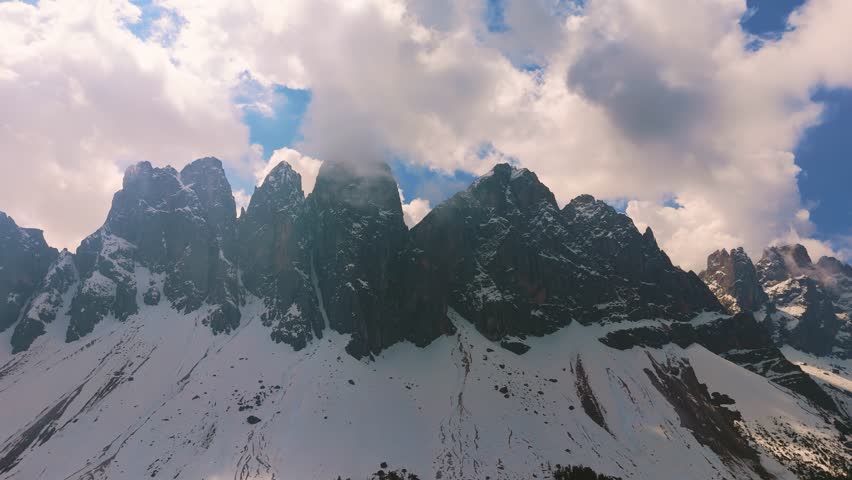 Snow covered Geisler peaks in Puez-Geisler Nature Park, Odle mountain range with clouds. Dolomites aerial