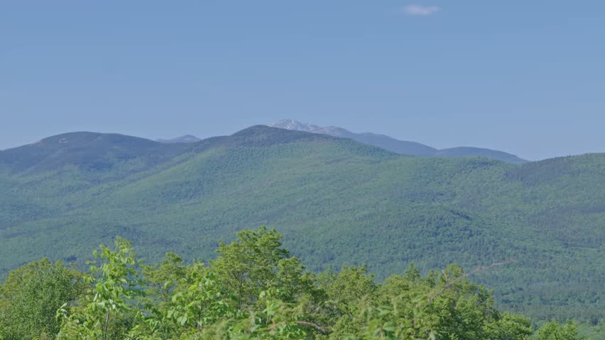 Distant view from Bear Notch Rd to snow-capped Mount Washington mountain range at White Mountain National Forest with dense forest beneath, New Hampshire, United States