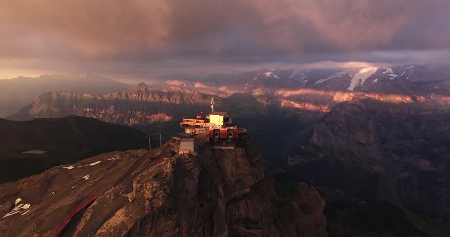 Aerial view of a mountain cable car station during sunset with dramatic clouds and scenic alpine landscape.