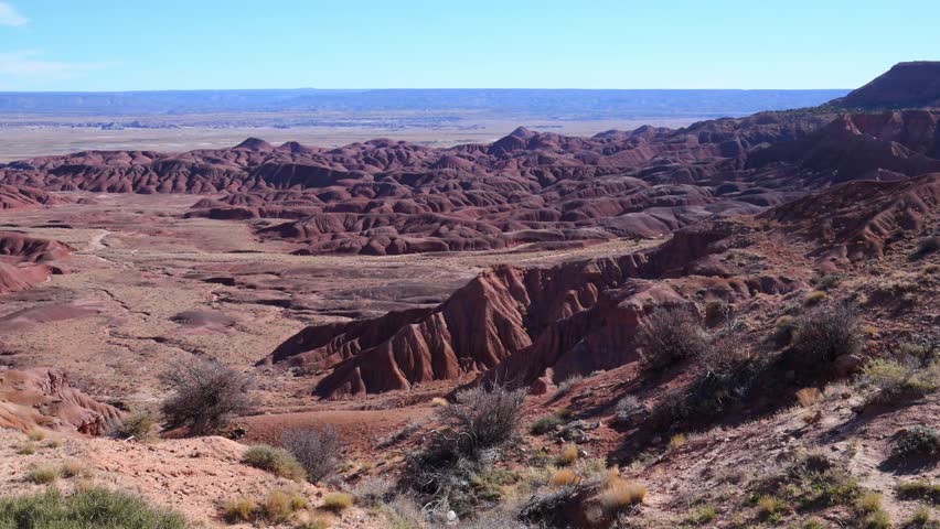 Arizona, USA. The rugged badlands of the Painted Desert within Petrified Forest National Park, Arizona. The landscape is characterized by intensely eroded hills and mesas composed of vividly colored, stratified sedimentary rocks in red, purple, and lavender hues. This arid desert region is renowned for scenic drives and hiking, with panoramic overlooks such as Tawa Point and Kachina Point offering expansive views of the multicolored geological landscape.