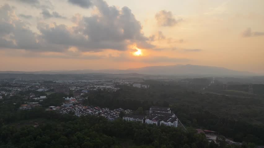 Aerial drone view of a dramatic sunset over a tropical landscape with residential area, forest and distant hills in Johor Bahru, Malaysia. Scenic evening sky captured from above in Southeast Asia