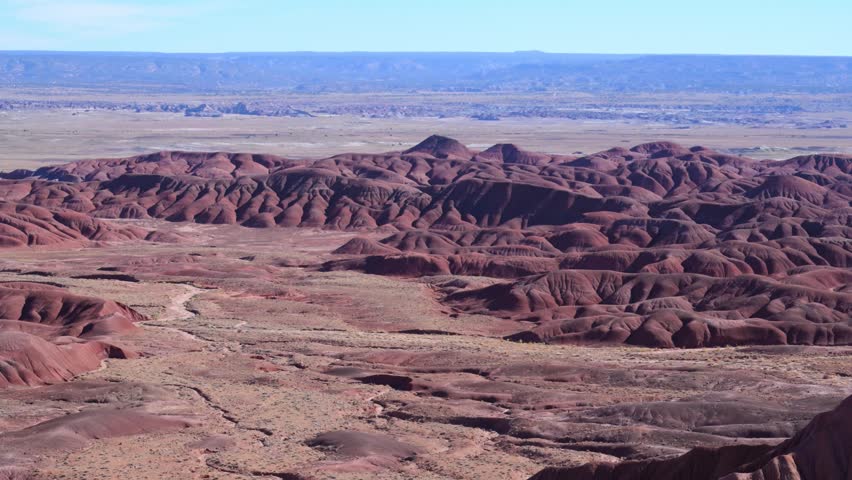 Arizona, USA. The rugged badlands of the Painted Desert within Petrified Forest National Park, Arizona. The landscape is characterized by intensely eroded hills and mesas composed of vividly colored, stratified sedimentary rocks in red, purple, and lavender hues. This arid desert region is renowned for scenic drives and hiking, with panoramic overlooks such as Tawa Point and Kachina Point offering expansive views of the multicolored geological landscape.