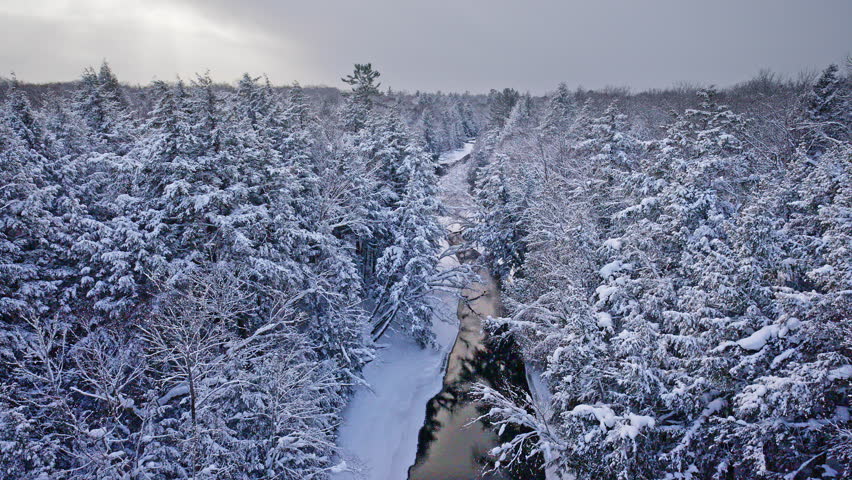 Stunning aerial view of a snow-covered woodland and winding river in Northern Michigan during winter.