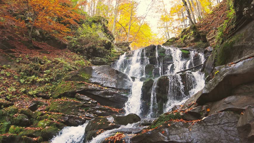 Waterfall falling down mountain slope in autumn forest