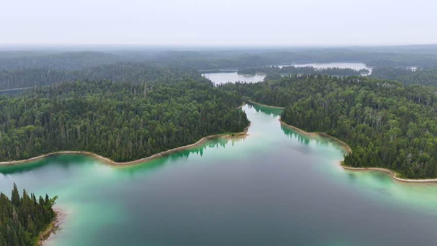Aerial view of a narrow water passage connecting two lakes through dense boreal forest at Arnott Lake in Northern Ontario beneath an overcast sky.