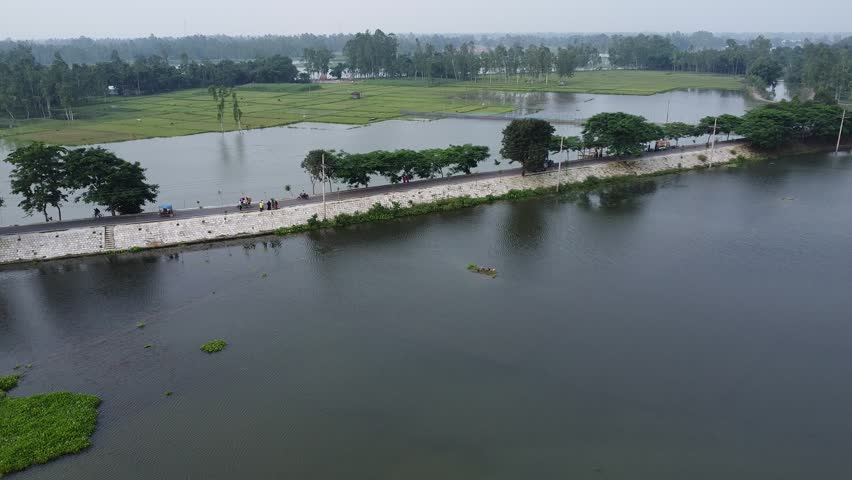 Aerial perspective of people walking on causeway between large ponds a high angle shot showing along a stone lined road situated calm lakes in rural environment