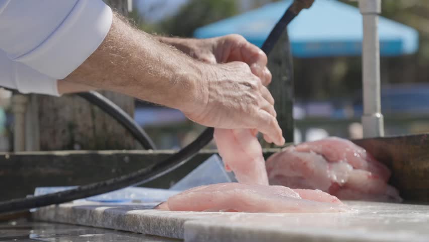 Person filleting fresh fish on cutting board in outdoor preparation area with knife