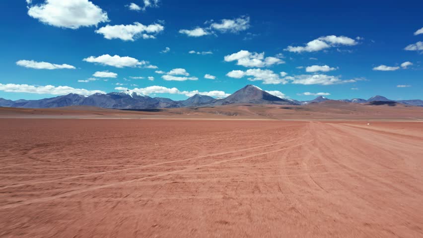 Aerial view of the vast Atacama Desert with rugged mountains under a bright blue sky with scattered clouds in San Pedro de Atacama, Antofagasta, Chile.