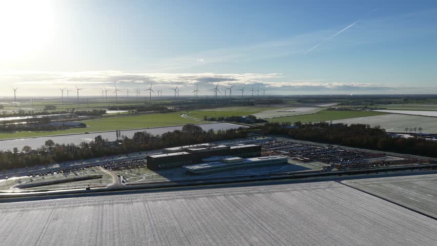 An aerial view of Ommelander Hospital in Groningen, The Netherlands, framed by frosted fields and distant wind turbines under soft sunrise light
