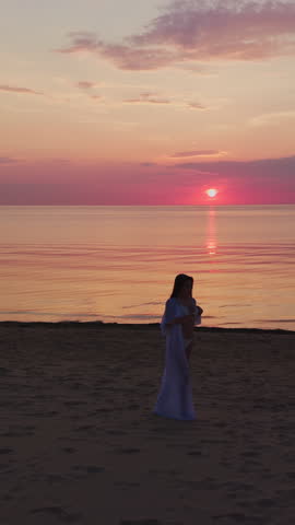 Silhouette of woman standing on quiet beach at sunset with glowing sky, calm sea, and warm pastel reflections