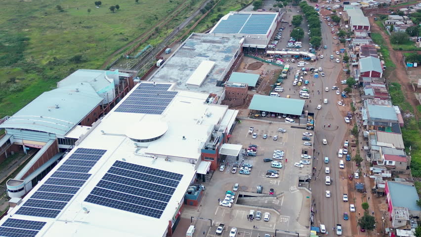 Solar-equipped township retail center and crowded street with parking lots seen in a daytime drone flyover.