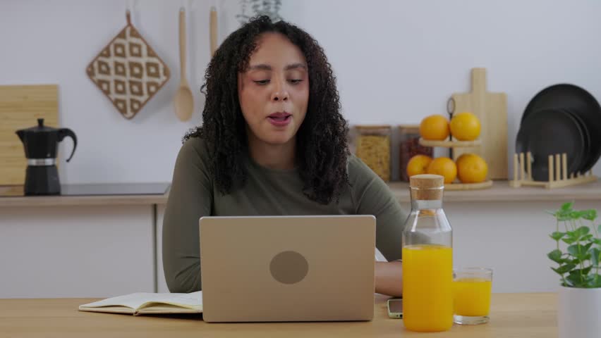 Young Brazilian student asking questions during online class. Female university student speaking with professor on video call while studying from home. Online education and distance learning concept.
