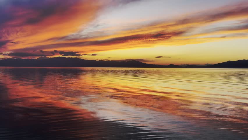 Vibrant sunset sky with fiery orange and purple clouds reflecting on smooth lake water ripples.
