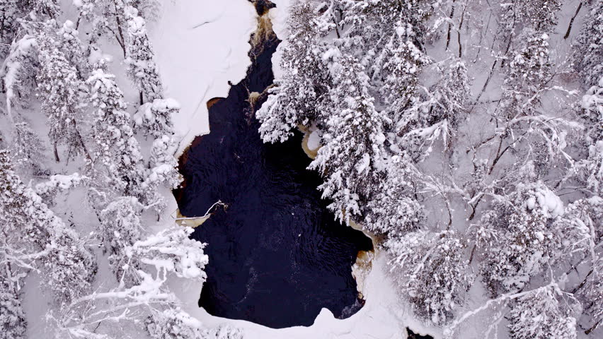 Relaxing aerial view of a snow-covered Northern Michigan forest with a gentle river winding through the landscape.