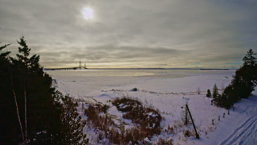 Drone view of the iconic Mackinac Bridge rising above snow-covered ice during a Northern Michigan winter.