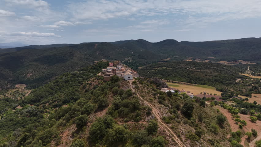 Flying across house of prayer on a mountain top with scenic Spanish village in the background. Pyrenees, Spain.