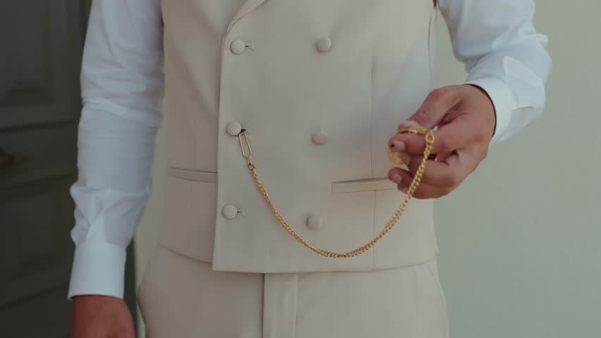 Man in cream waistcoat tucking a gold pocket watch chain into pocket