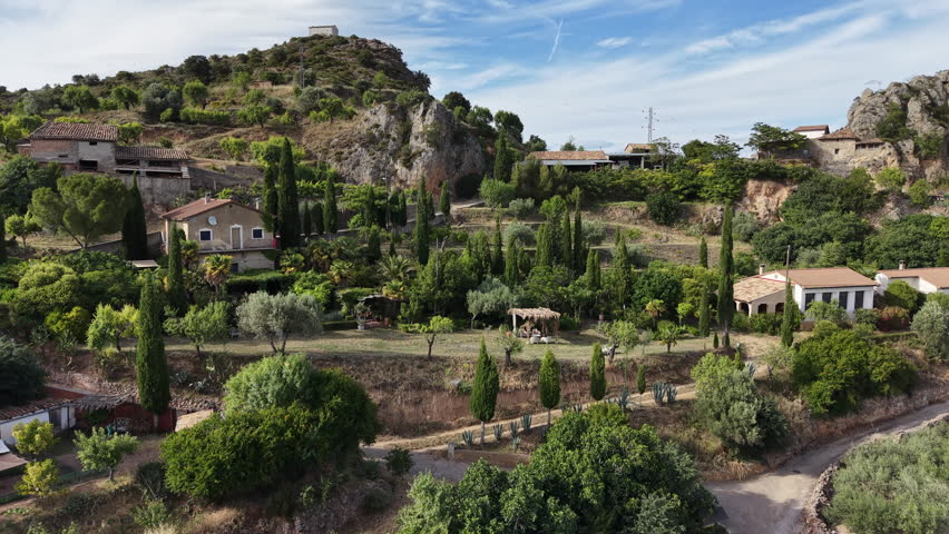 Aerial shot of beautiful garden and houses in a scenic Spanish village in the Pyrenees. Camera approaches and rises to reveal vast landscape behind mountain.