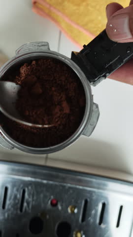 A top-down close-up view of a barista using a metal coffee tamper to press down freshly ground coffee inside a portafilter basket during the espresso preparation process