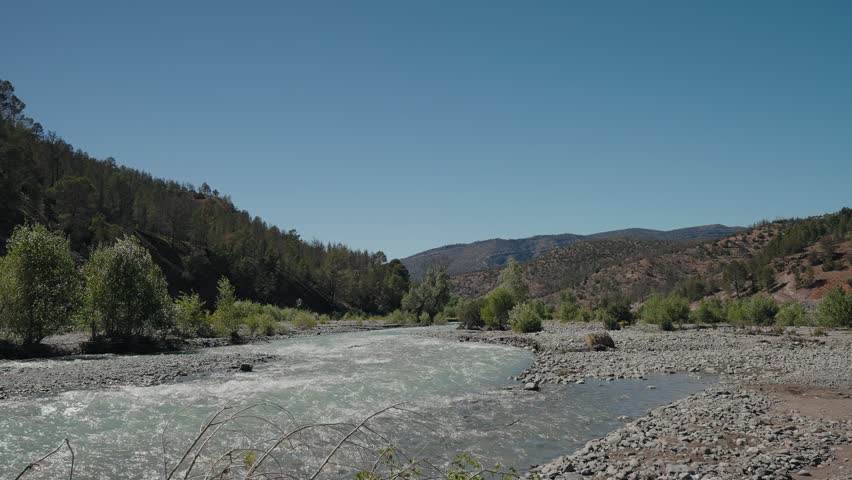 Fast flowing mountain river over rocky bed with forested hills in Atlas Mountains Morocco