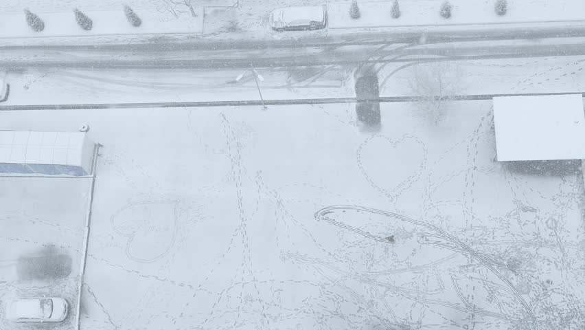 Aerial top-down view of a young boy sledding and sliding on deep snow, leaving curved tracks during a winter snowfall in slow motion.