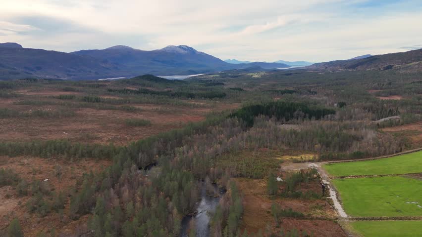 An aerial view of forest and marshland near Lake Fosterlagen in Gjemnes, Norway, with distant mountains rising under soft daylight