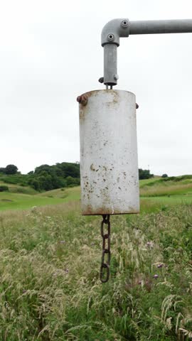 Person ringing an old rusty metal bell in a field