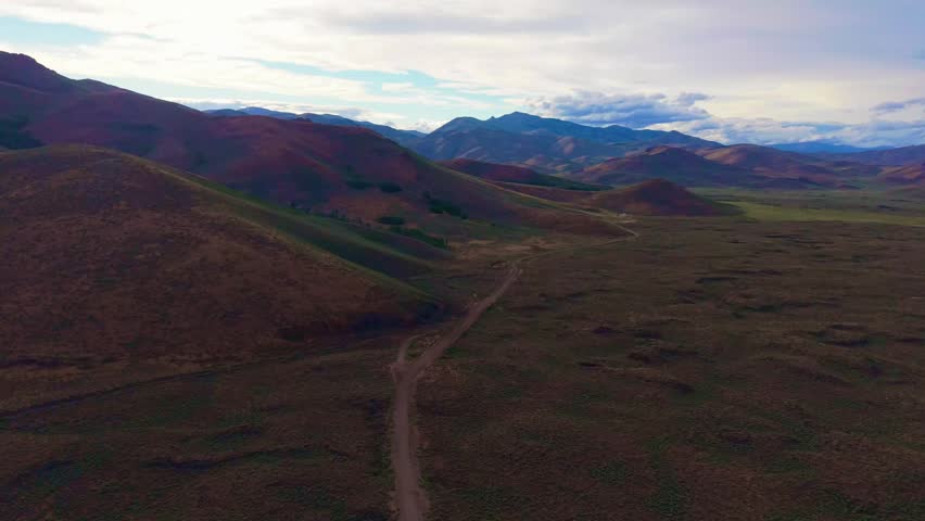 Golden sunset light traces a lonely winding road through rolling hills of rural Idaho