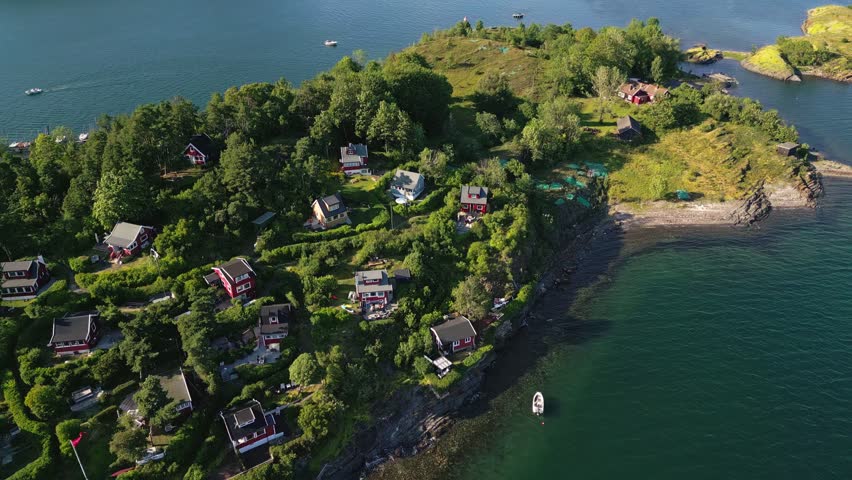 Aerial view of red wooden cabins nestled among trees on a rocky island surrounded by the blue waters of the fjord in Oslo, Oslo, Norway.