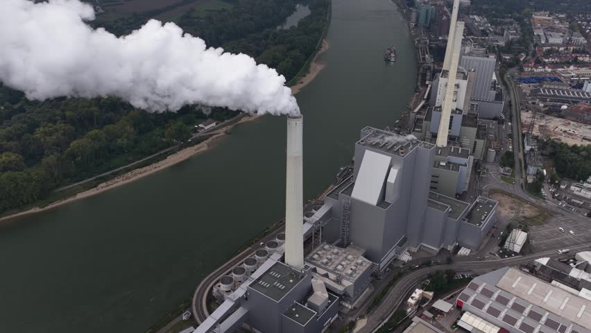 An aerial view of the Mannheim Power Plant in Germany, showing steam rising from the main stack along the Rhine and the vast industrial energy site