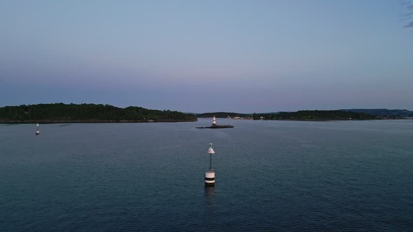 Aerial view of a navigation buoy in the foreground and a distant lighthouse on a small island in the calm waters of the Oslofjord Oslo, Oslo, Norway.