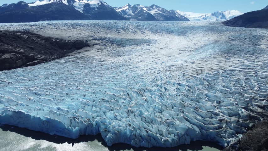 A drone shot of Grey Glacier in Torres del Paine stretches across a vast valley, its jagged blue ice glowing under clear southern skies