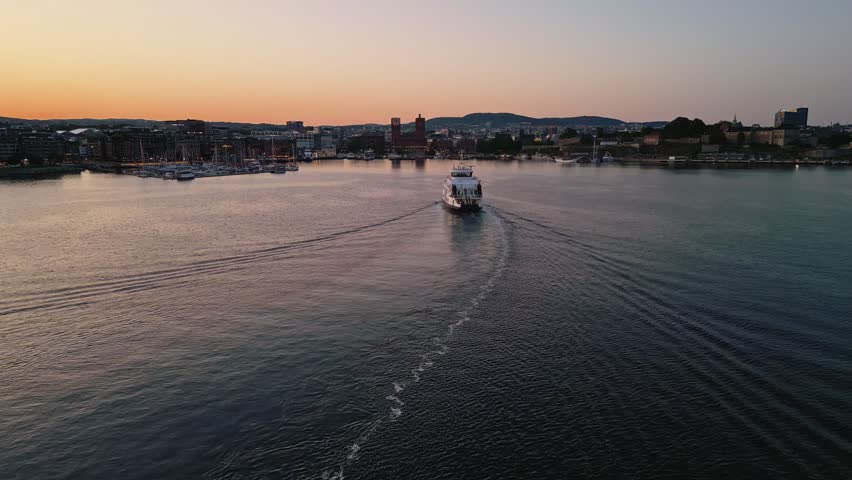 Aerial view of a ferry moving through the calm waters of the Oslo Fjord at sunset with the city skyline in the background in Oslo, Oslo, Norway.