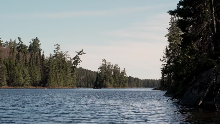 A calm forest lake stretches between tree-lined shores under a pale sky with gentle rippling water
