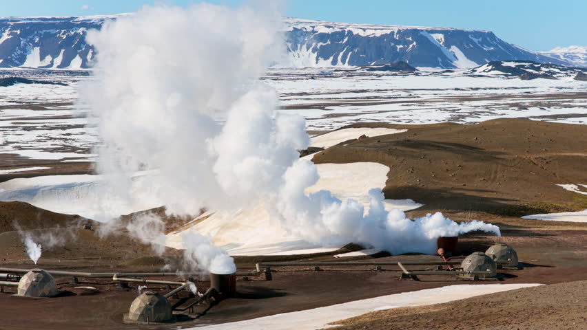 Steam emanates from volcanic site. Vast geothermal installation amid volcanic and mountain scenery