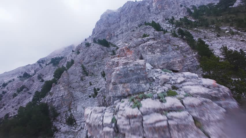 Breathtaking FPV drone ascent soaring up the narrow limestone ridge of Mount Olympus into thick drifting clouds. The dynamic first-person flight skims low over rugged mountain trails, capturing high-altitude alpine majesty