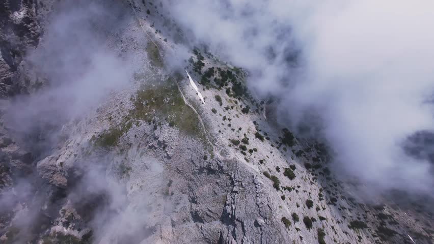 Cinematic FPV drone shot diving rapidly along the sharp crest of Mount Olympus in Greece. Immersive action footage plunging down a rocky mountain path into thick white fog and deep alpine valleys