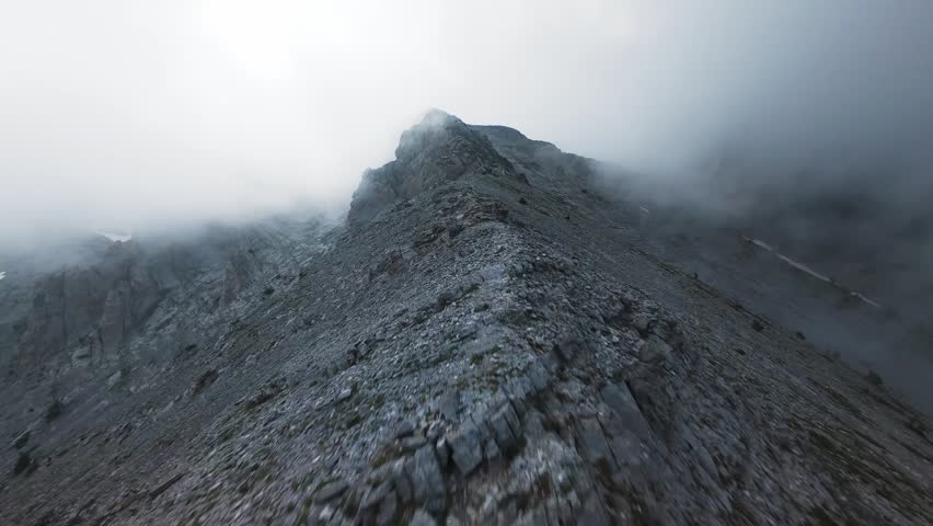 Breathtaking FPV drone ascent soaring up the narrow limestone ridge of Mount Olympus into thick drifting clouds. The dynamic first-person flight skims low over rugged mountain trails, capturing high-altitude alpine majesty