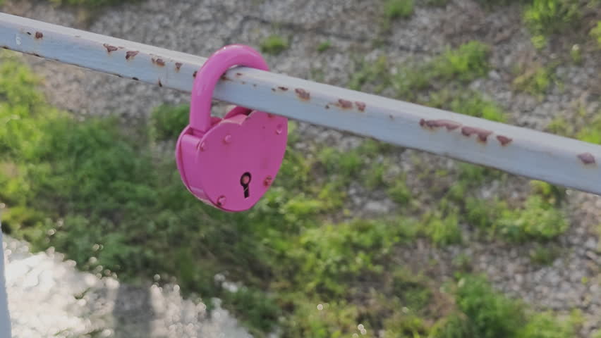 Pink heart shaped love padlock hanging on a rusty bridge railing as a symbol of eternal romance