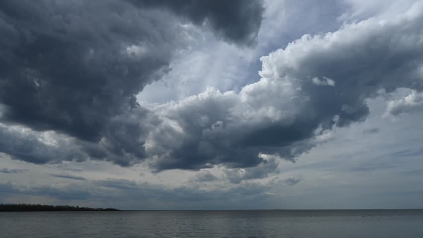 Time-lapse of storm clouds drifting across the sky above a large lake with trees along the horizon